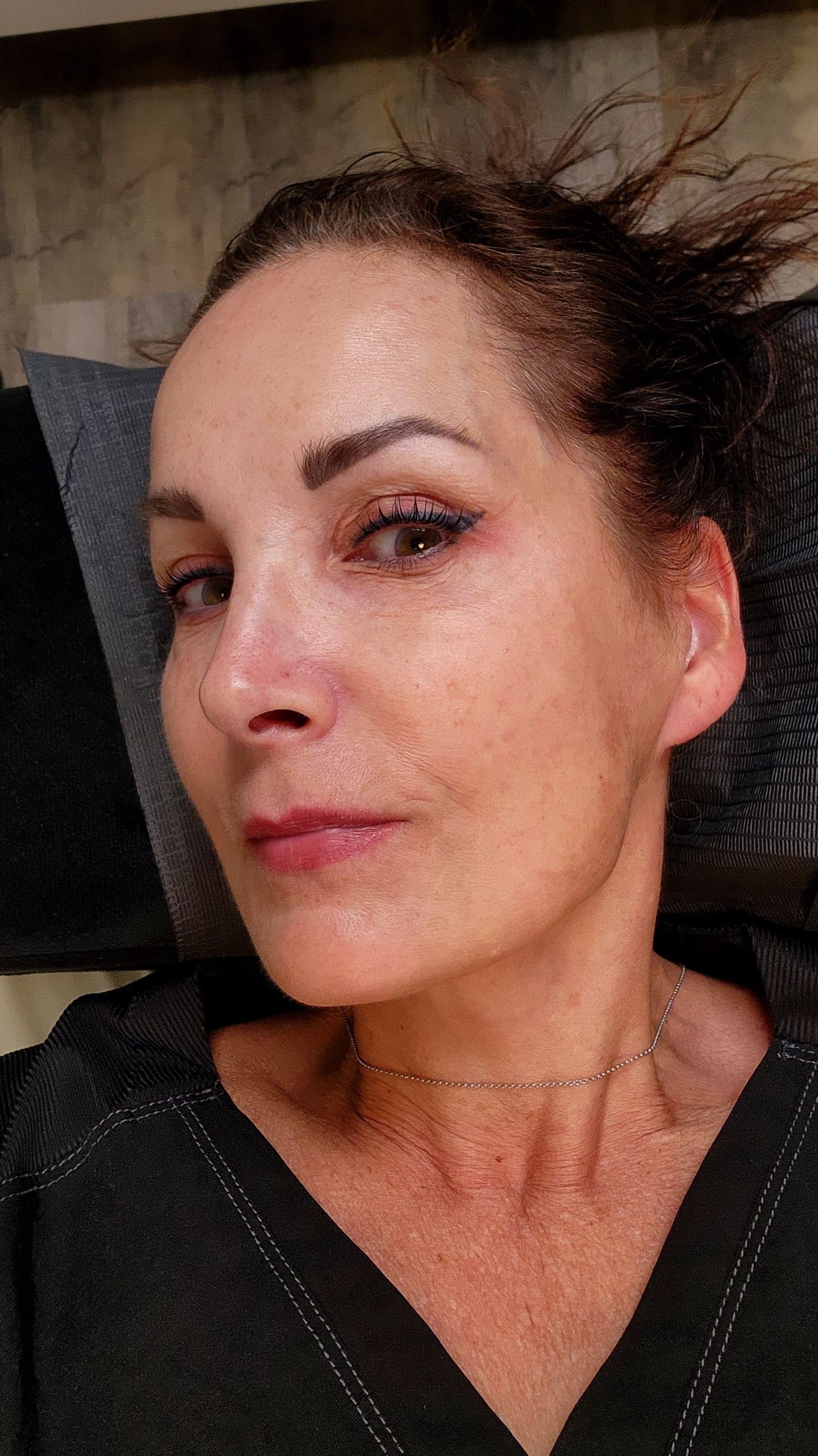 Woman with dark hair and makeup, looking at the camera. She's wearing a dark shirt, and a gold necklace.