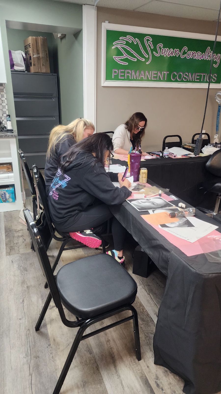 Three people working at a table with materials. A sign for