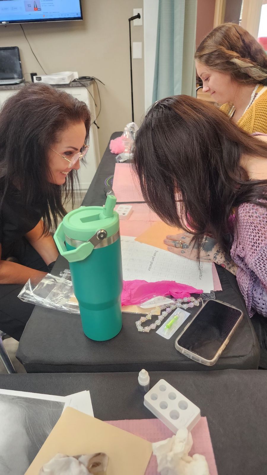 Three women looking at documents spread on a table. A teal water bottle and other items are on the table in front of them.