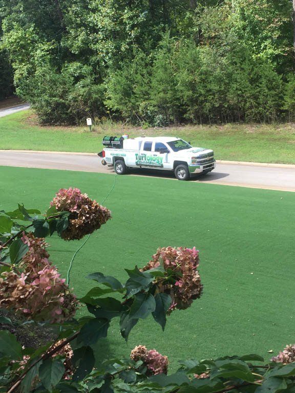 A white truck is driving down a road next to a lush green field.