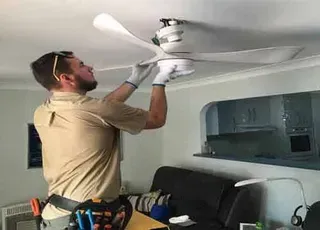 A man is installing a ceiling fan in a living room.