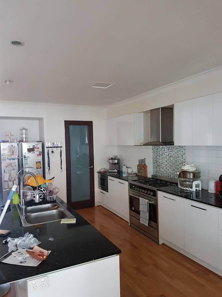 A kitchen with white cabinets , black counter tops , a stove , a sink , and a refrigerator.