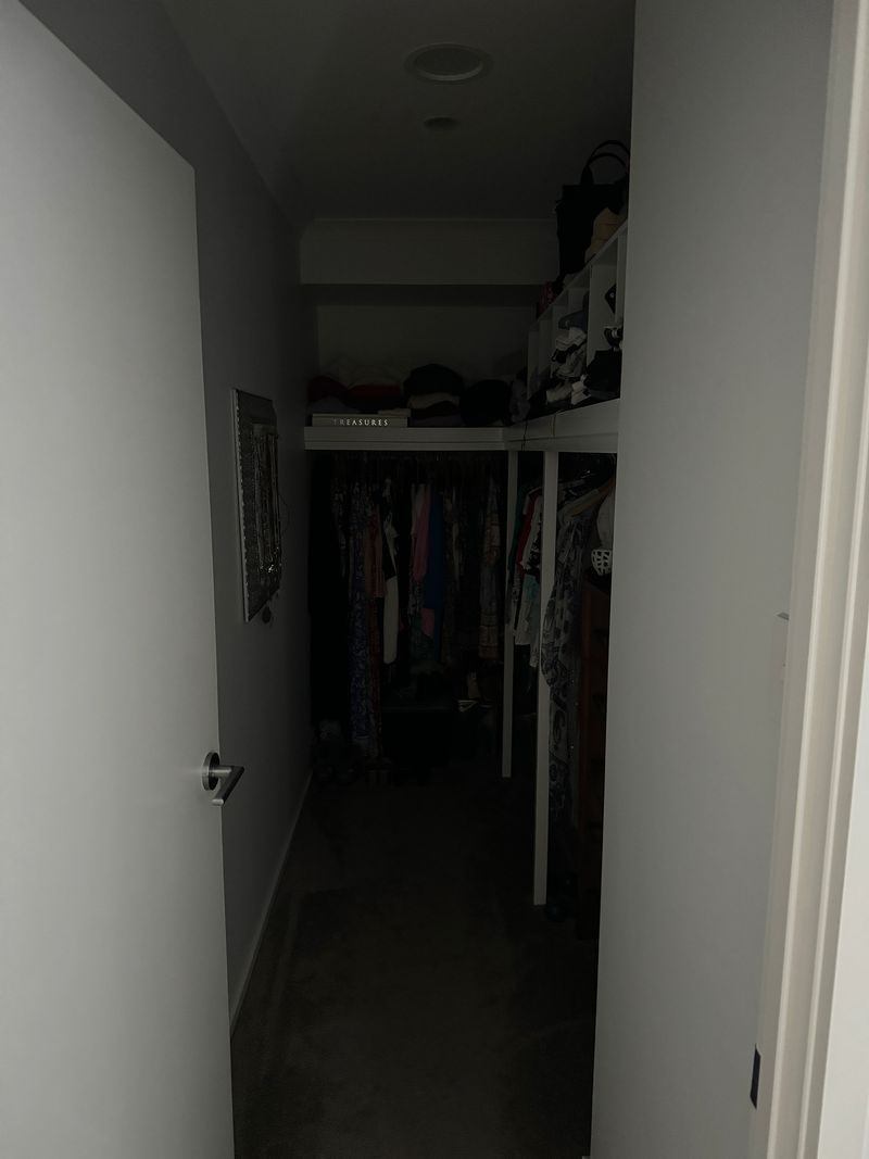 A dark hallway with a door open and a closet filled with clothes.