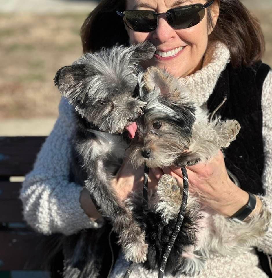 A woman wearing sunglasses is holding a small dog