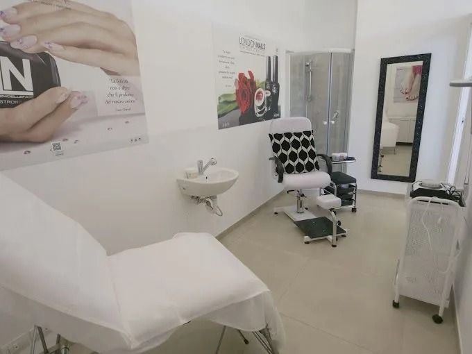 Interno di un salone per unghie con poltrona reclinabile, postazione per pedicure, lavandino, specchio e poster dei prodotti.