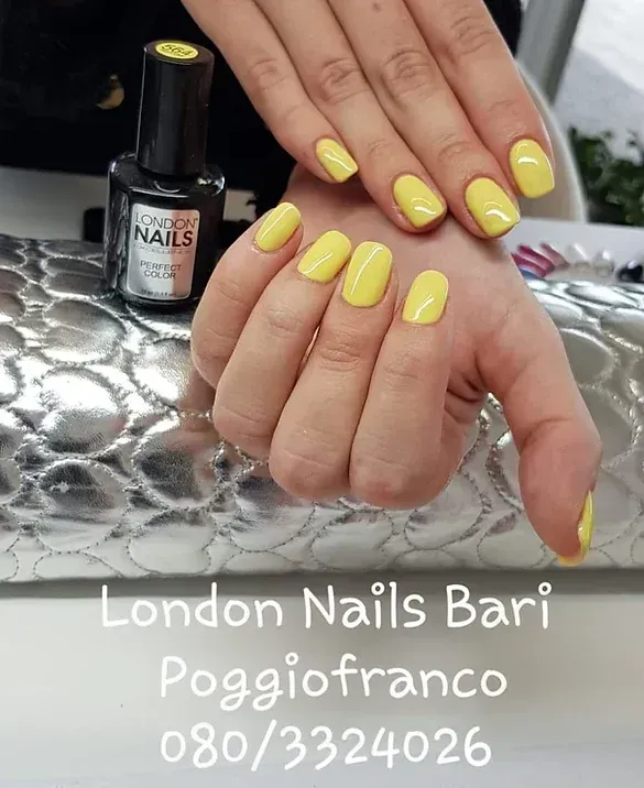 Manicure gialla sulle mani, London Nails Bari, boccetta di smalto, superficie argentata.