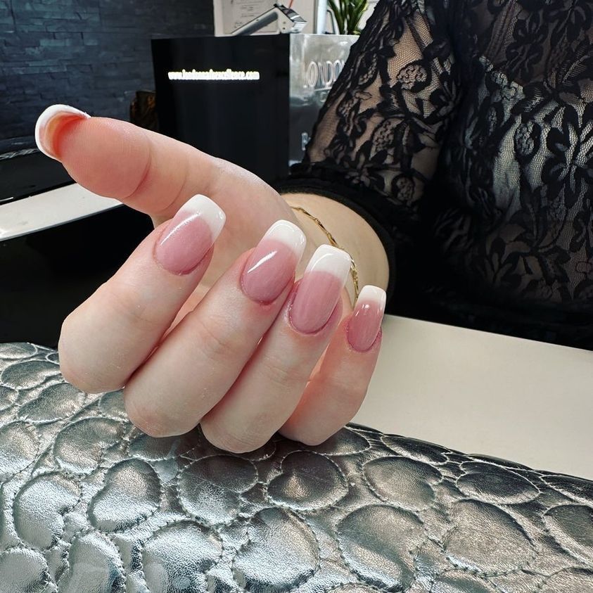 Mano con french manicure su una superficie decorata con motivi argentati; manica in pizzo nero sullo sfondo.