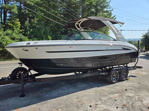 White and black motorboat on a trailer, parked on a road with trees in the background.
