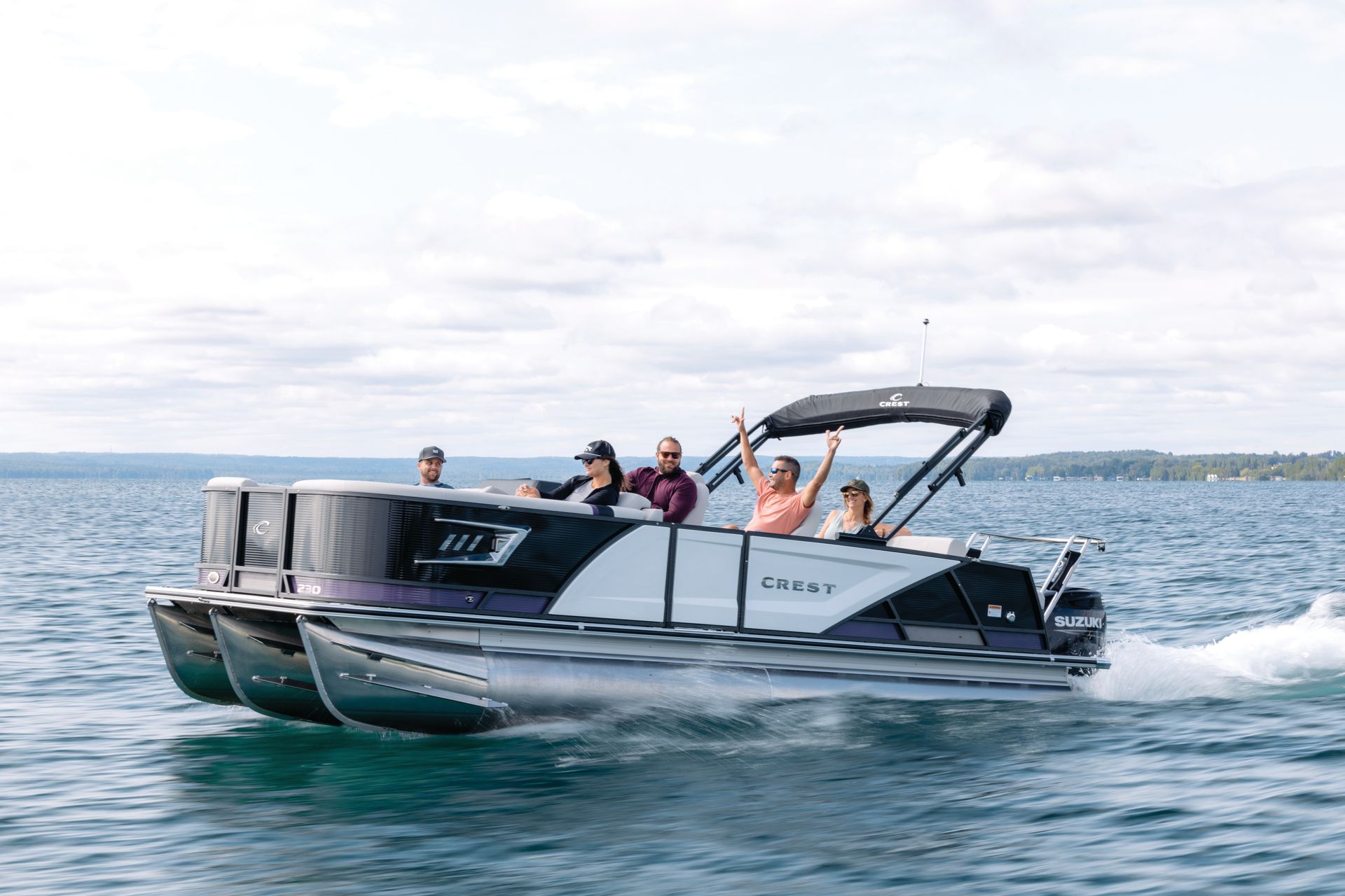 Pontoon boat with five people on a lake, waving, sunny day.