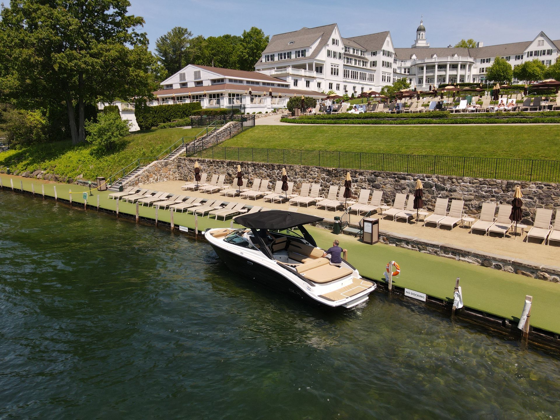 Boat docked at a resort on a lake, with lounge chairs and buildings in the background on a sunny day.