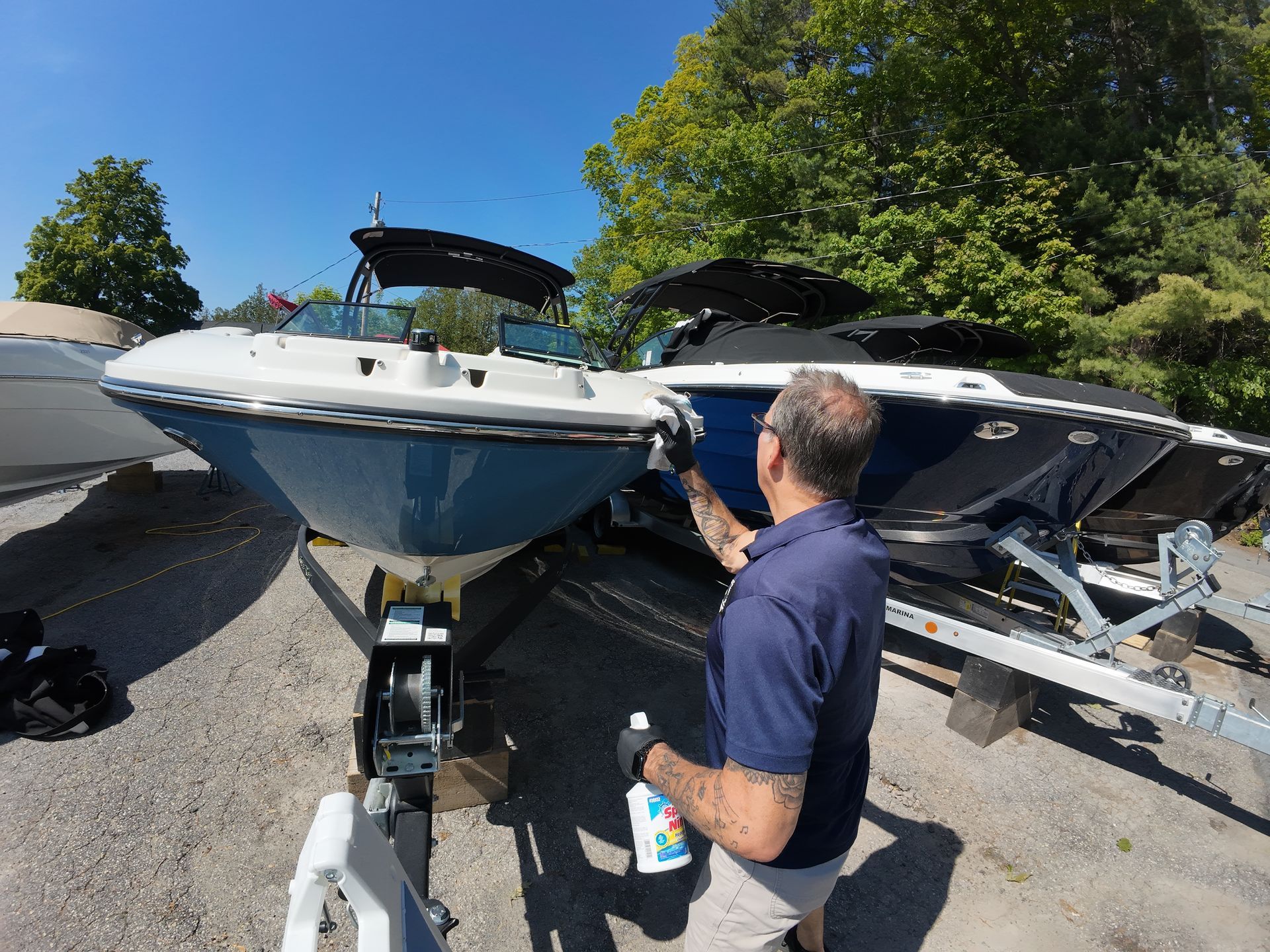 Man cleaning a blue and white boat on a trailer, sunny day.