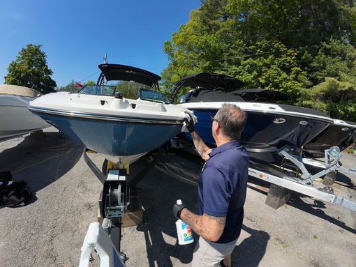 Man cleaning a blue and white boat on a trailer, sunny outdoor setting.