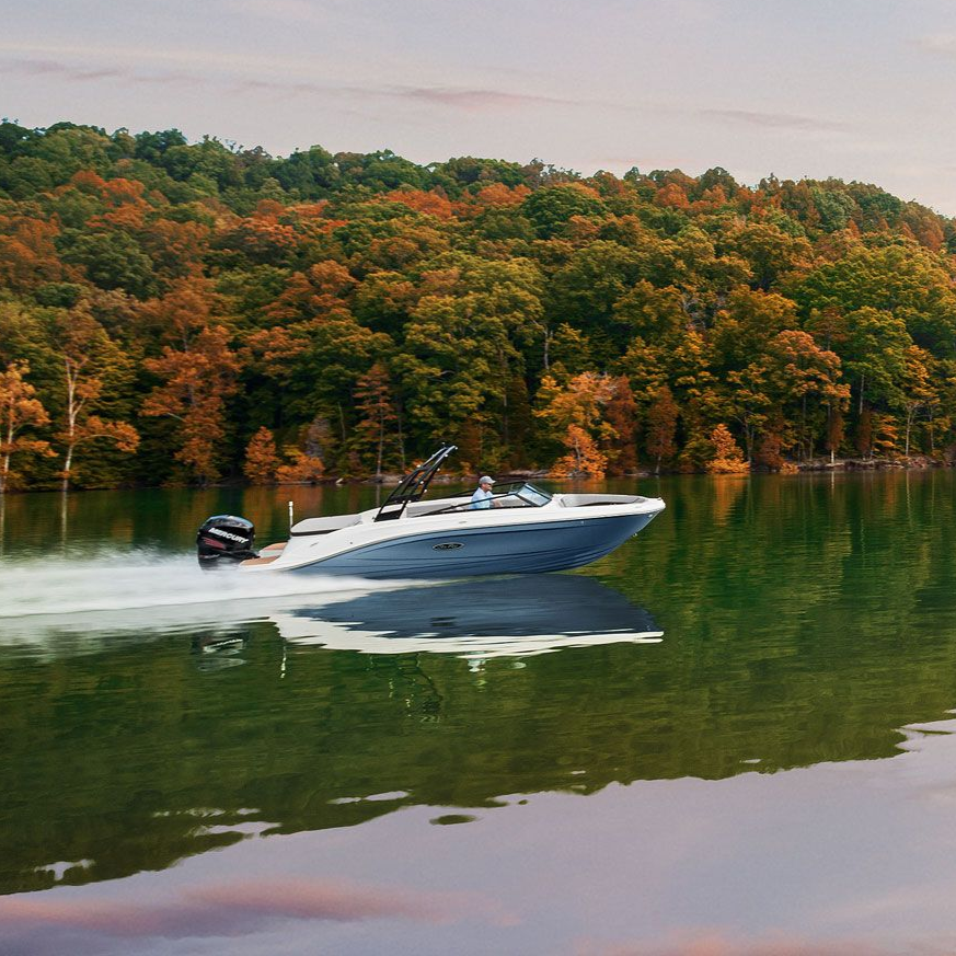 A motorboat speeds across a lake with fall foliage in the background.