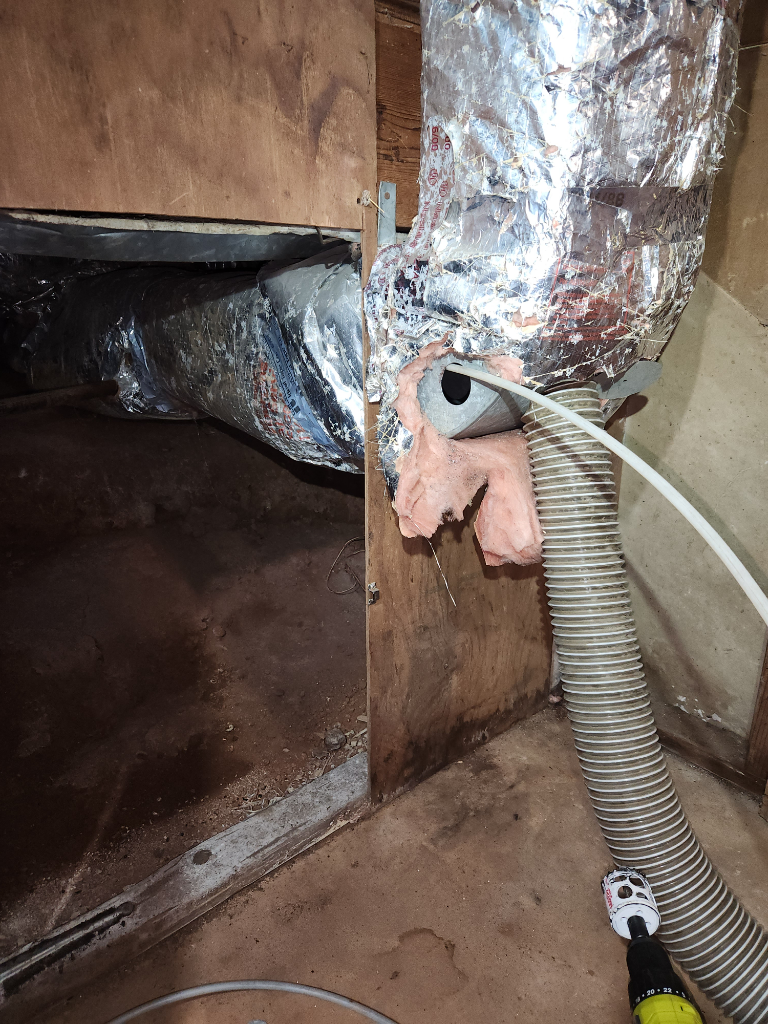 A vacuum cleaner is being used to clean a duct in a basement.