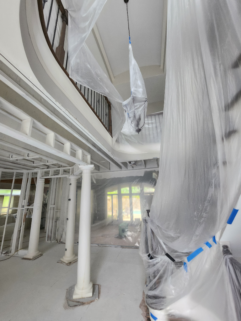 A large room with a staircase and columns is being painted.