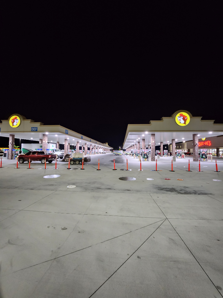 A lot of cars are parked in a parking lot at a gas station at night.