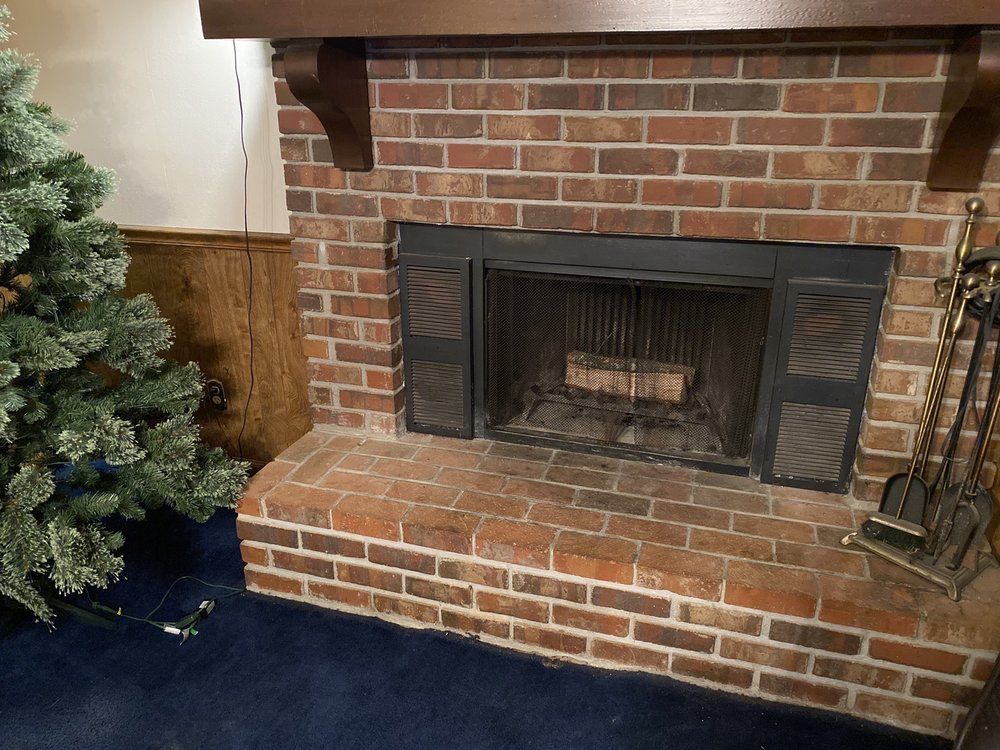 A brick fireplace in a living room next to a christmas tree.