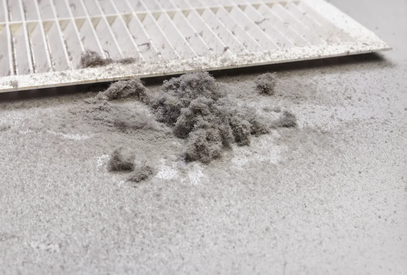 Dirty air filter and dust pile on a gray surface.