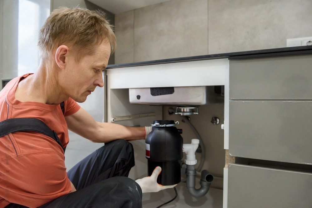 a man is fixing a garbage disposal in a kitchen .