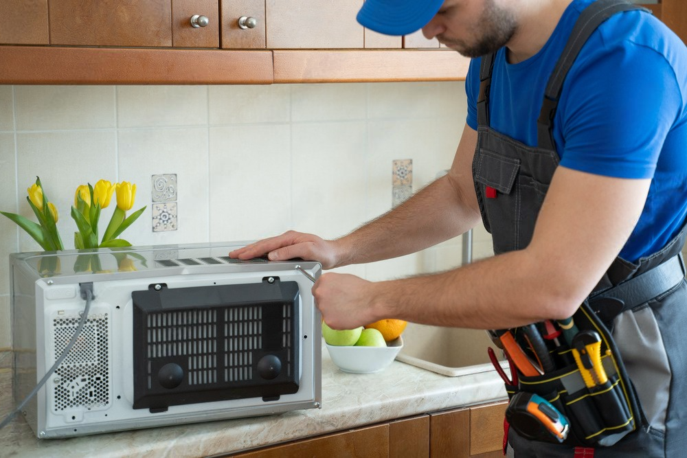 a man is fixing a microwave in a kitchen .