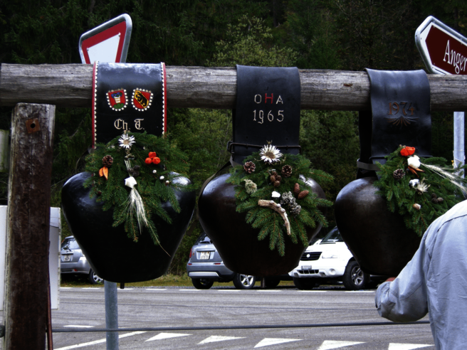 Drei Glocken hängen an einem Holzpfosten mit einem Schild mit der Aufschrift „Cha 1565“