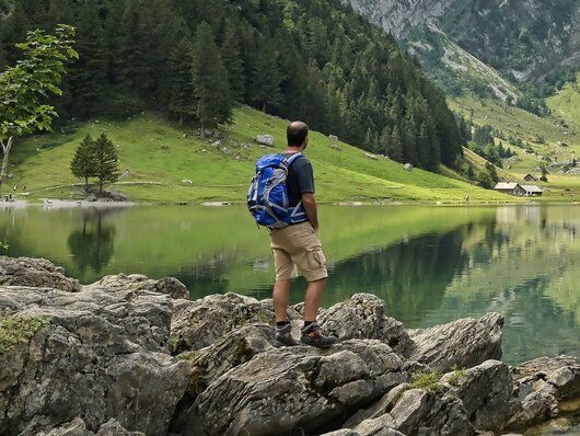 Ein Mann mit einem Rucksack steht auf einem Felsen in der Nähe eines Sees.