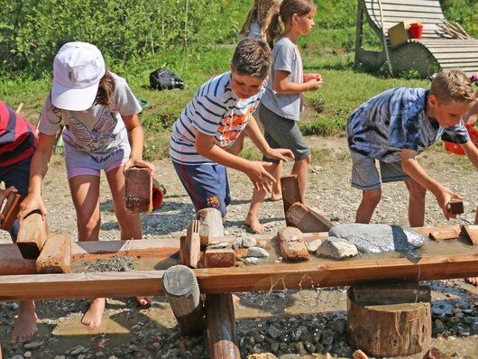 Eine Gruppe Kinder spielt mit einem hölzernen Wasserfall.