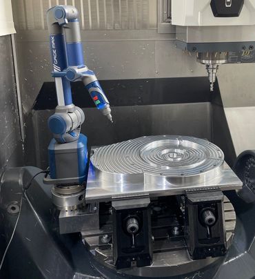 Ein blauer Roboterarm untersucht ein silbernes, kreisförmiges Metallteil auf einer CNC-Maschine.