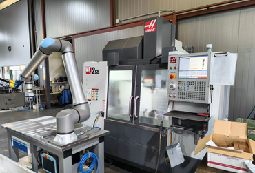 Ein Roboterarm arbeitet in einer Werkstatt mit einer CNC-Maschine.