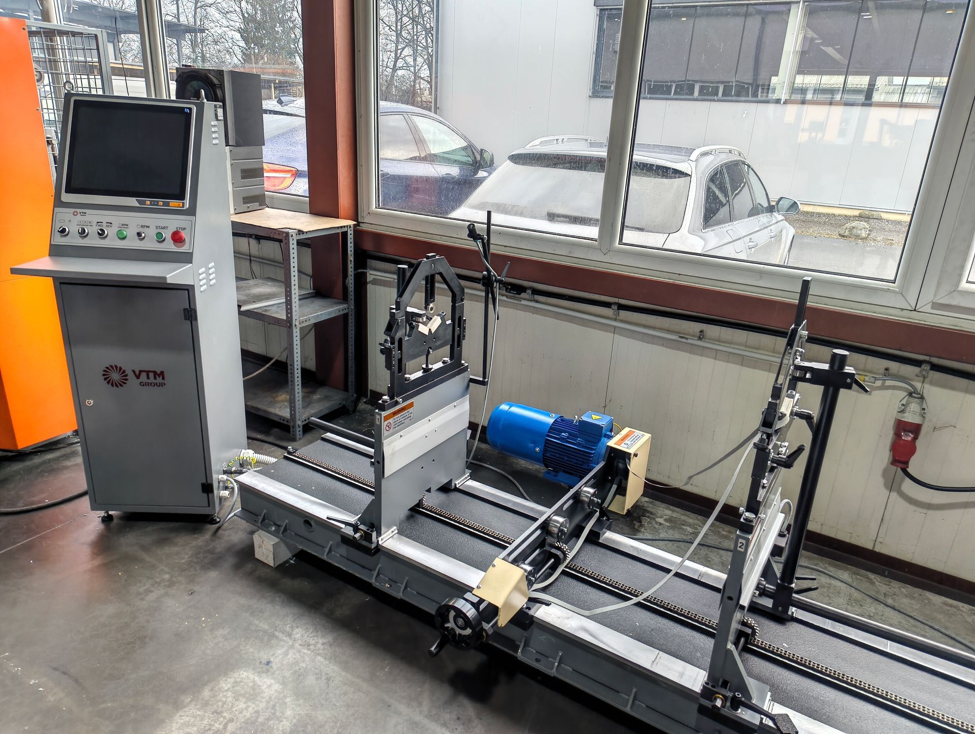 Orange und graue Metallbiegemaschine mit Bedienfeld und Fußpedal in einer Fabrikumgebung.