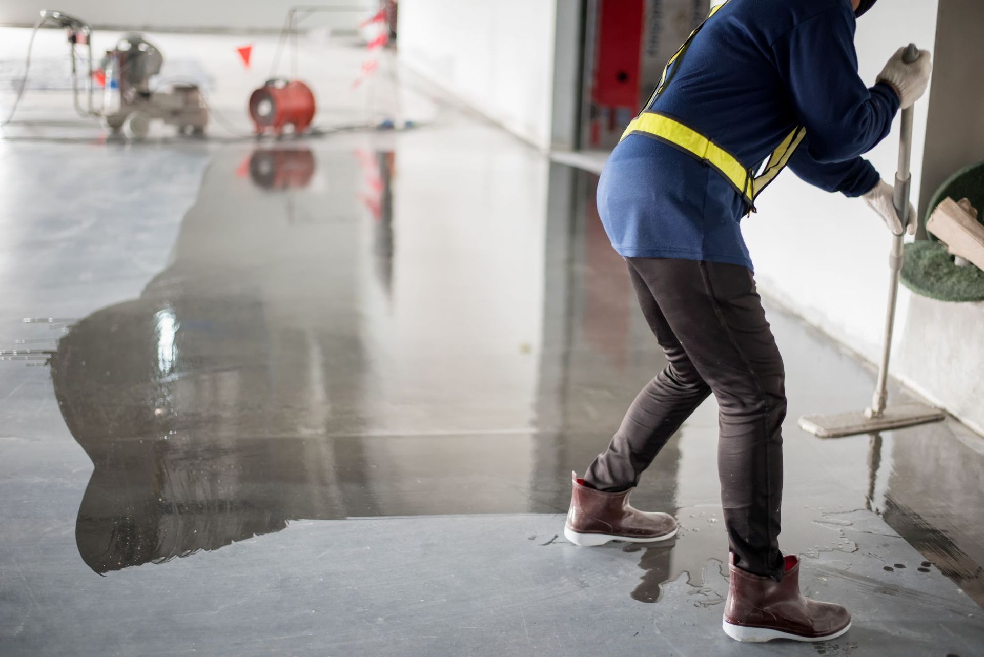Person squeegeeing water from a wet concrete floor in an indoor industrial space