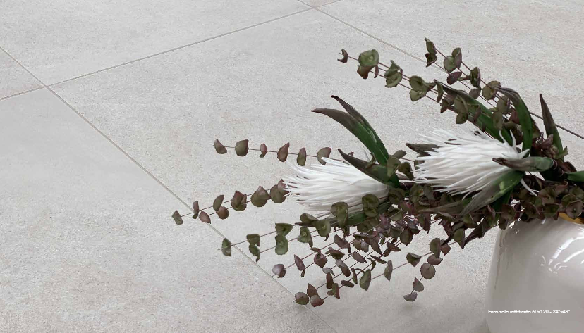 Close-up of a white vase with eucalyptus and protea against light gray tiled floor.