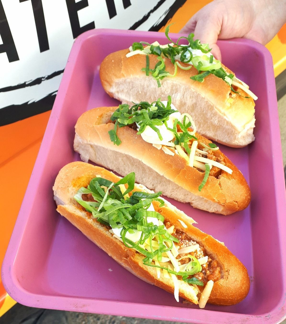 Three Loaded Hot Dogs in Pink Tray, Topped With Onions — Mels Catering in Julia Creek, QLD