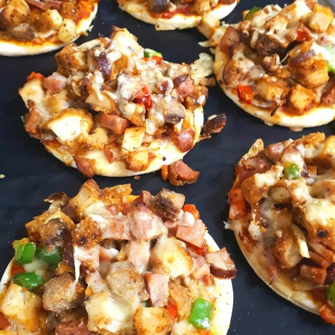 Mini pizzas with various toppings, including chicken, ham, peppers, and cheese, on a dark surface.— Mels Catering in Garbutt, QLD