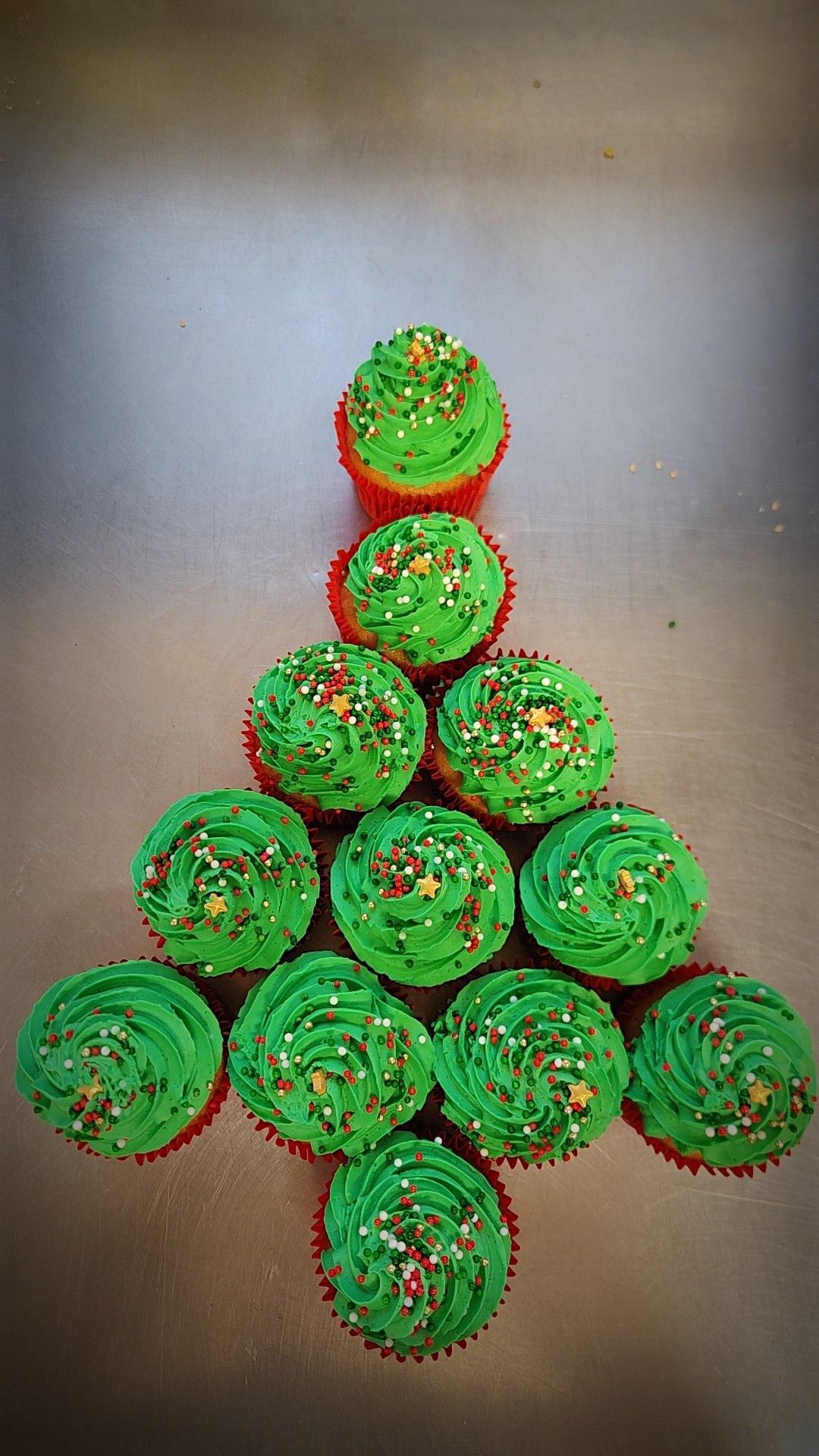 Cupcakes arranged in a Christmas tree shape, green frosting with sprinkles, red liners.— Mels Catering in Garbutt, QLD