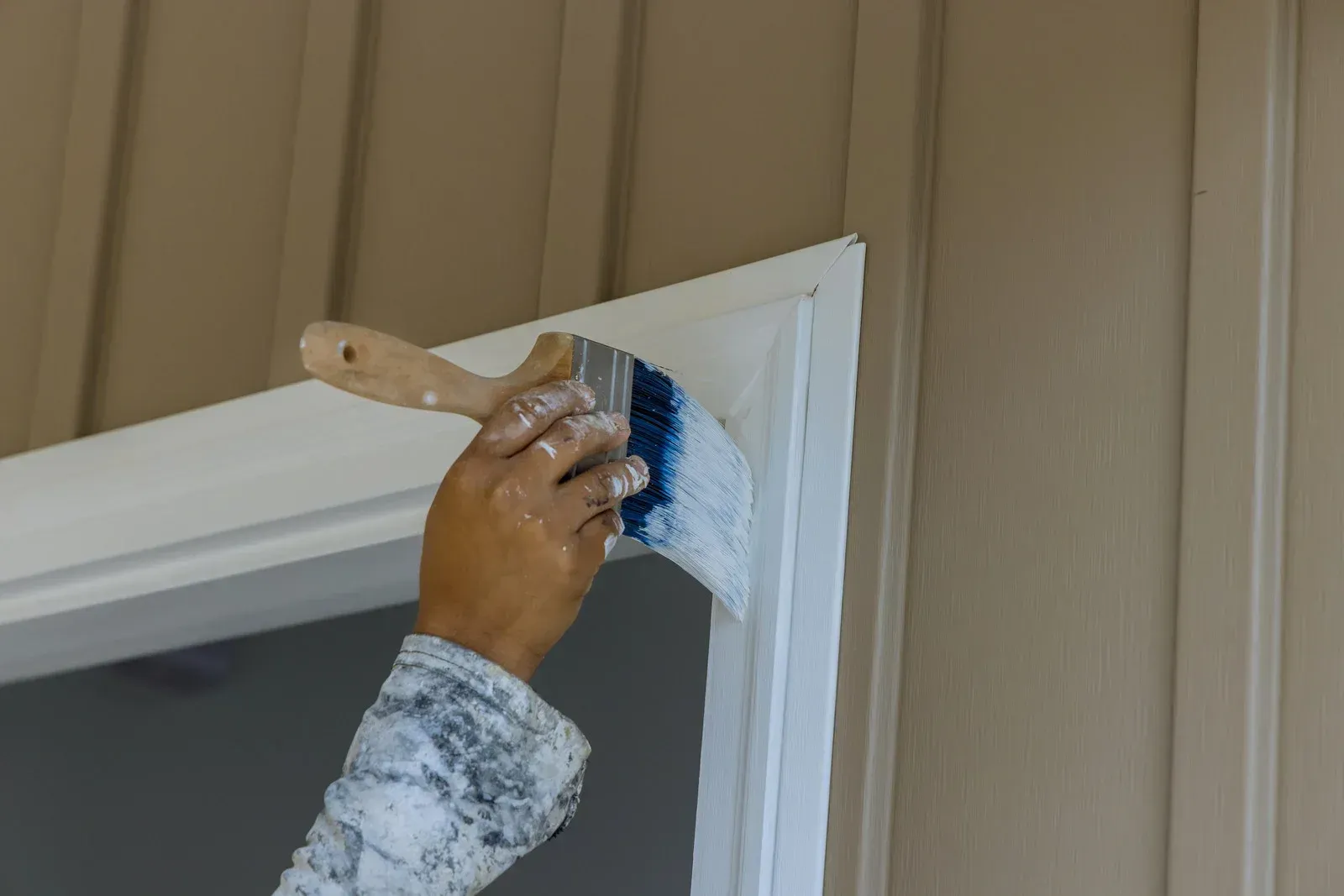 Person painting white paint onto a door frame with a brush.