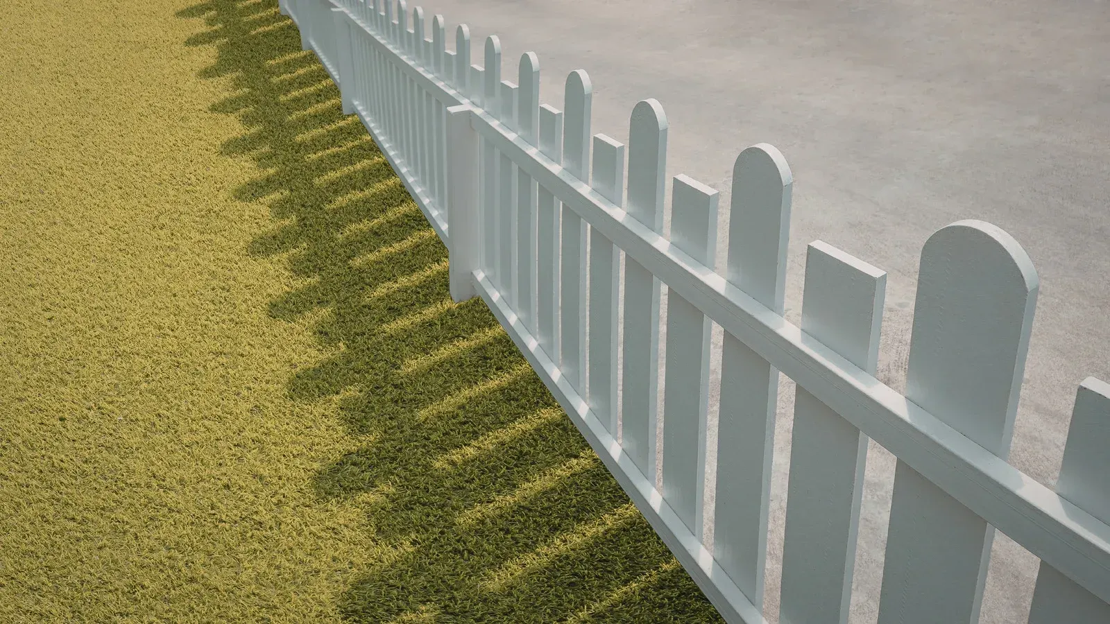 White picket fence casting long shadows on grass and pavement.