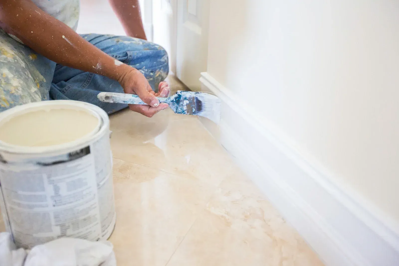 Hands in gray gloves applying painter's tape to a wall, between a green ceiling and light wood paneling.
