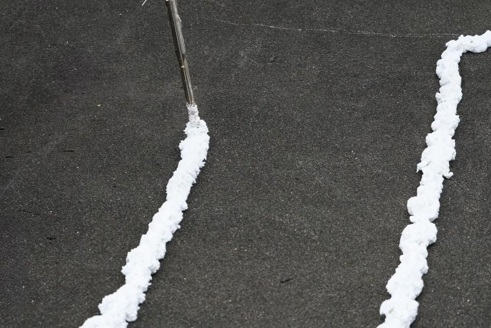 Two lines of white foam are being sprayed on a black surface.