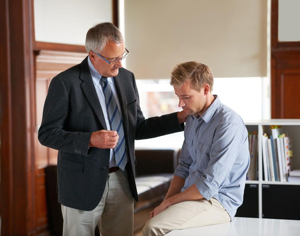 Man comforted by another man in an office, one with hand on shoulder.