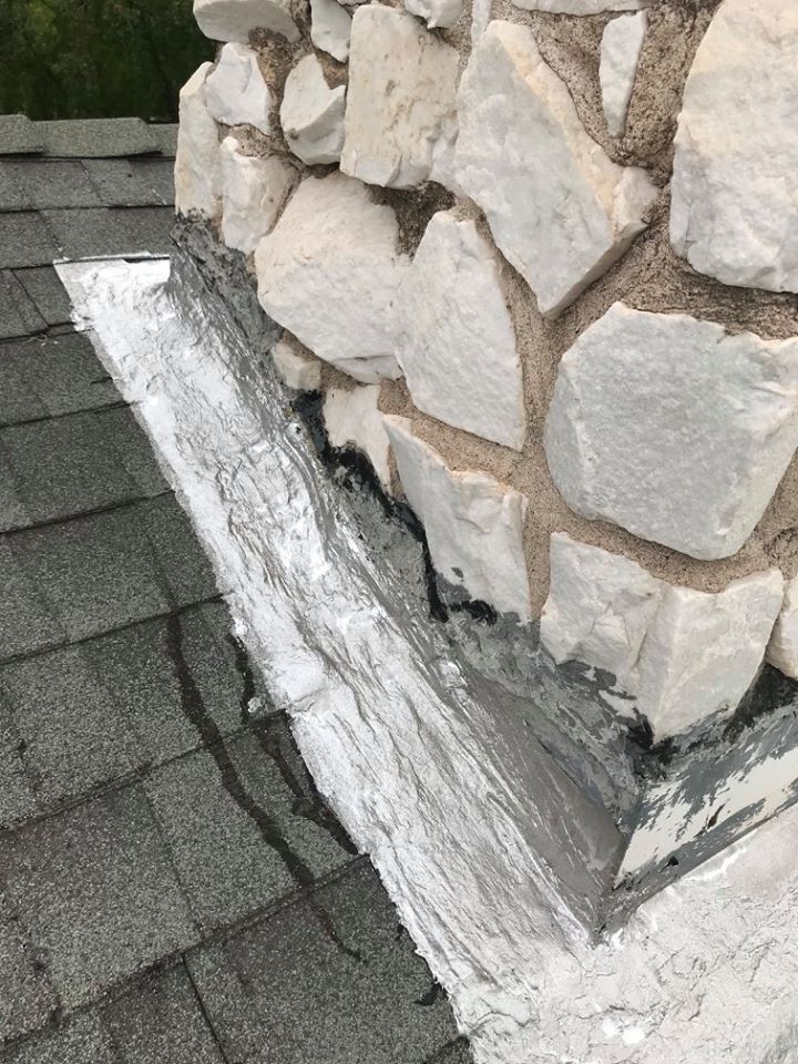 A chimney is sitting on top of a roof next to a stone wall.