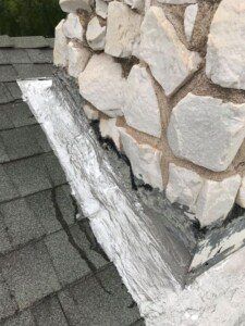 A close up of a chimney on a roof next to a stone wall.