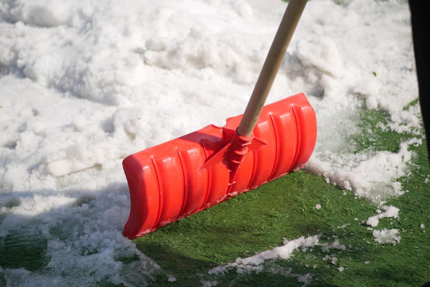 Red snow shovel on a patch of green turf covered in snow.