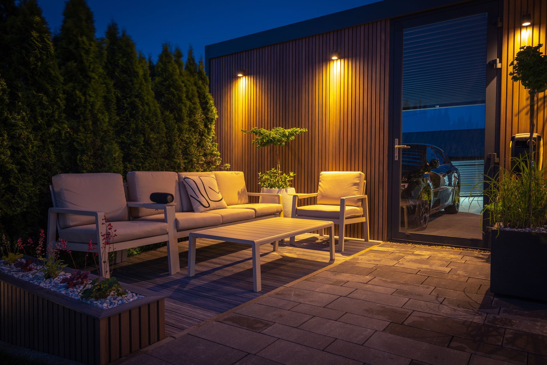 Outdoor patio lit at night, featuring a seating area and surrounding greenery.