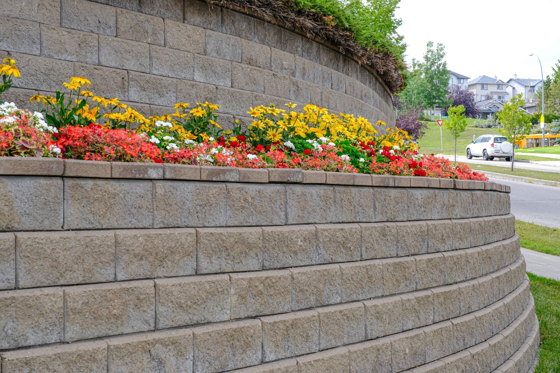 Curved retaining wall with colorful flowers alongside a road.