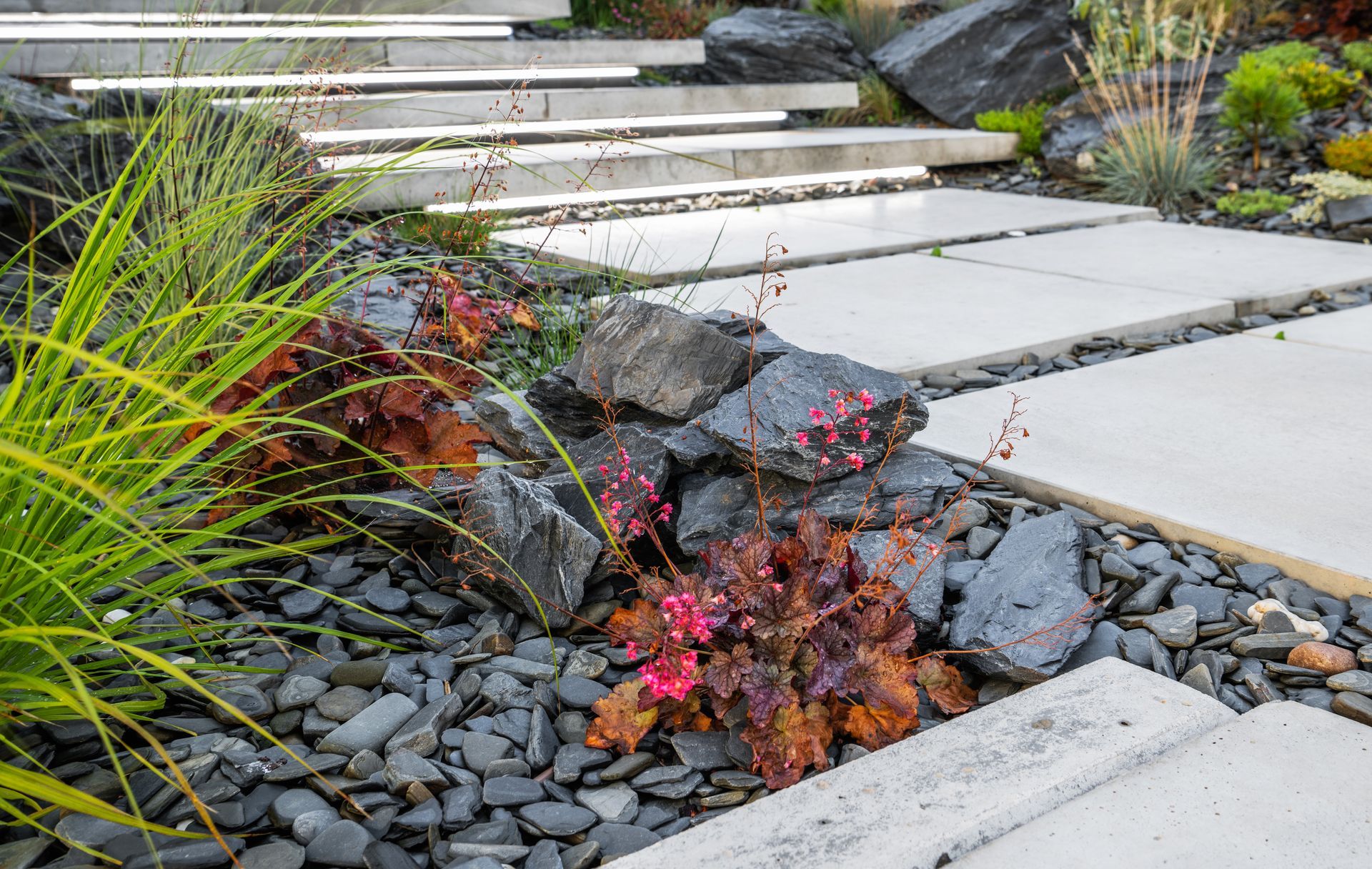 Stone steps and pathway with LED lighting, surrounded by a rock garden with plants and dark gravel.