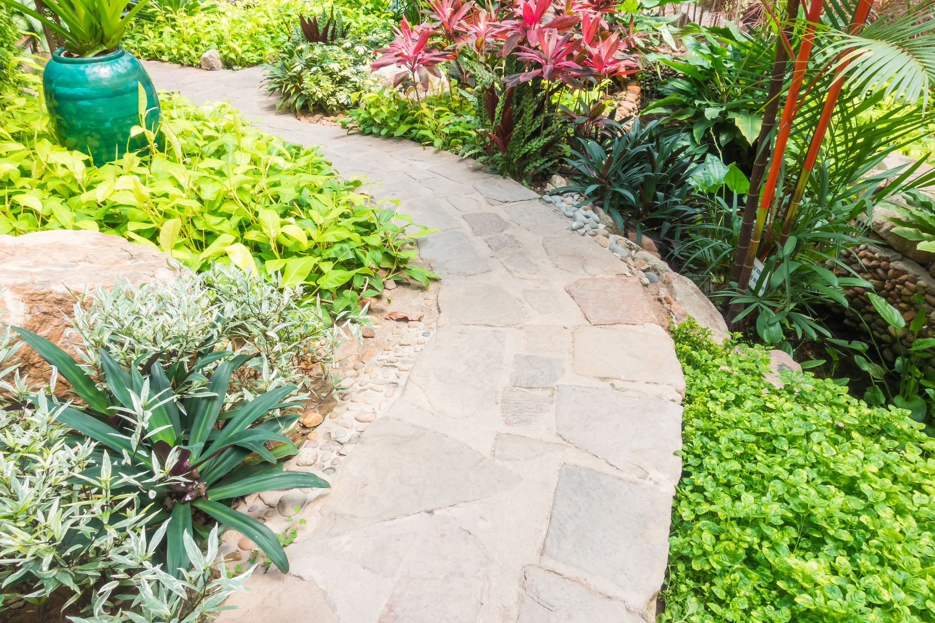 A stone walkway in a garden surrounded by plants and flowers.