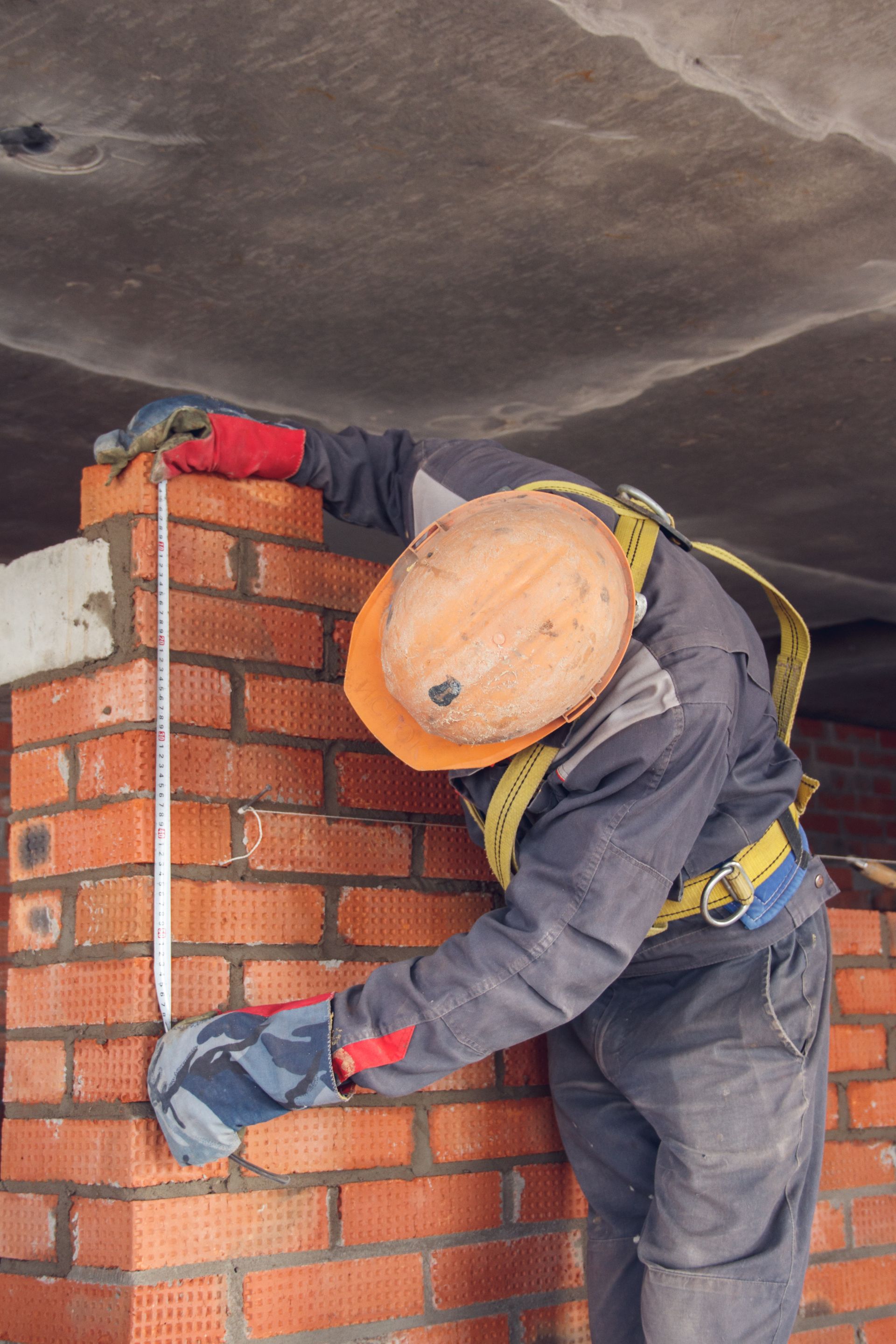 A construction worker is measuring a brick wall with a tape measure.