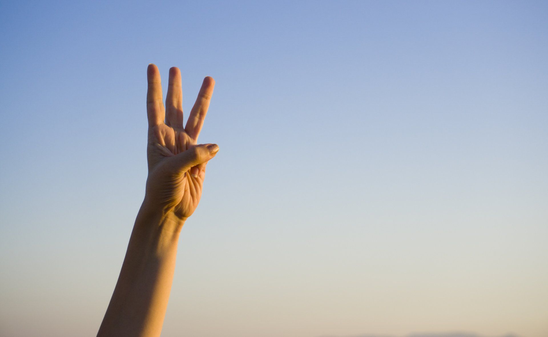 A person 's hand is making a peace sign against a blue sky.