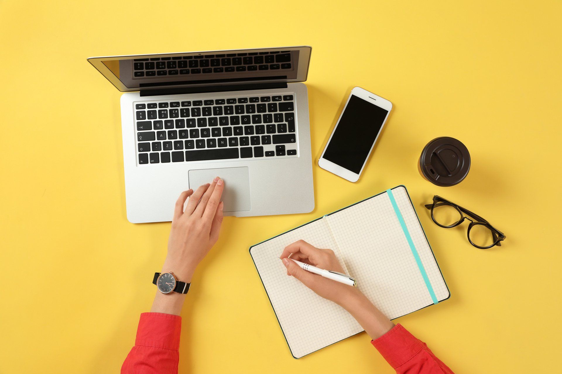 A person is using a laptop computer while writing in a notebook.